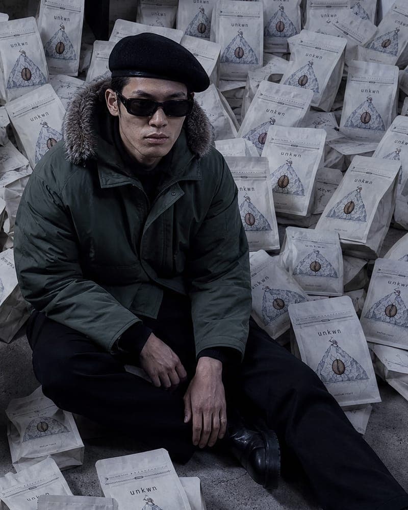 Seated figure in a green parka and beret, campaign still