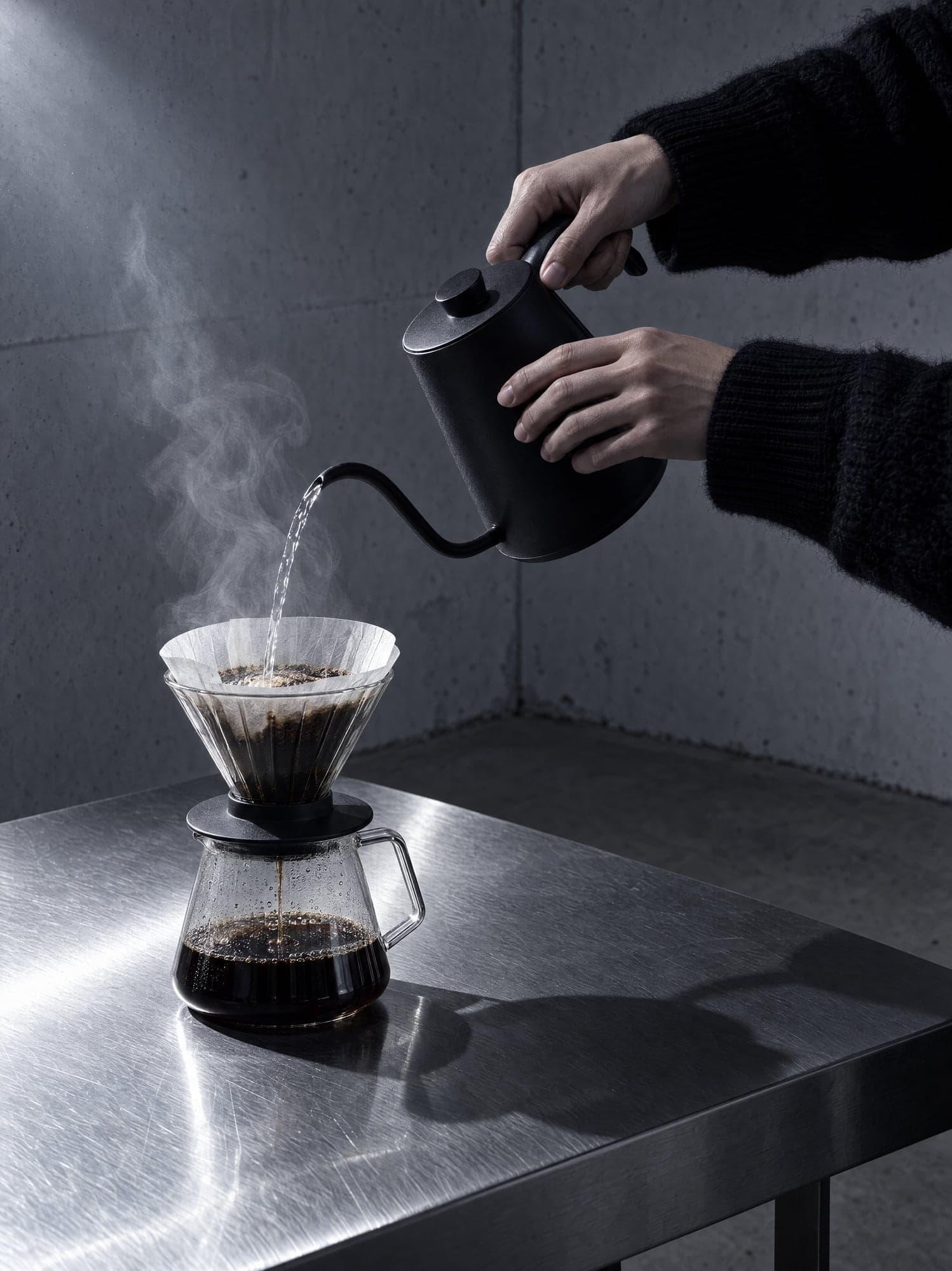 Hands pouring from a black kettle into a filter cone